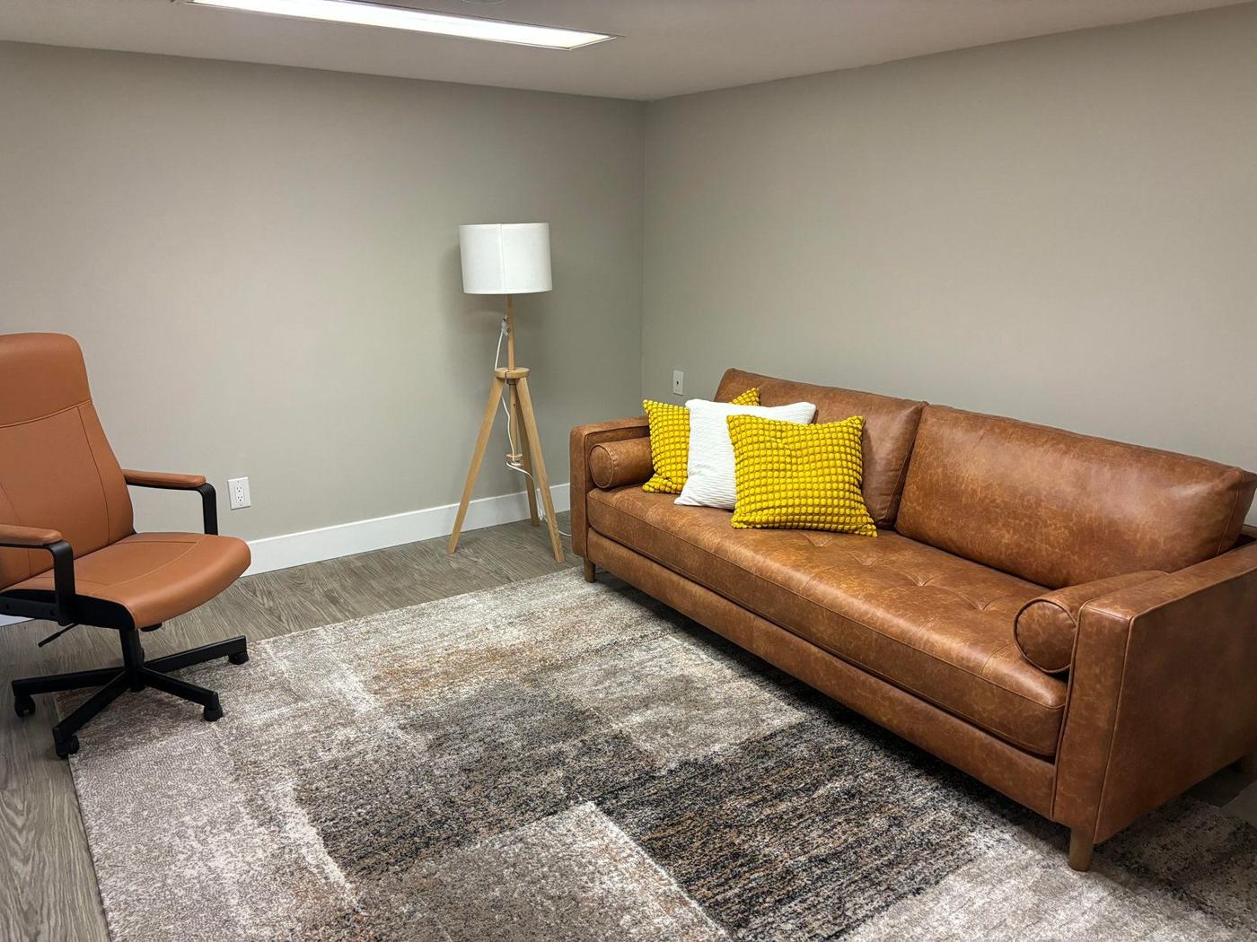 A quiet counselling room with a leather couch, yellow cushions, an armchair and a floor lamp