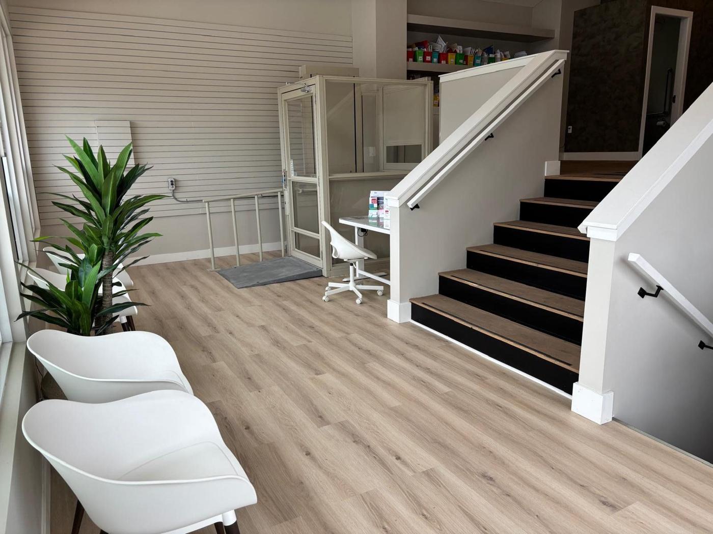 The entry with white chairs, a plant, a lift and a staircase