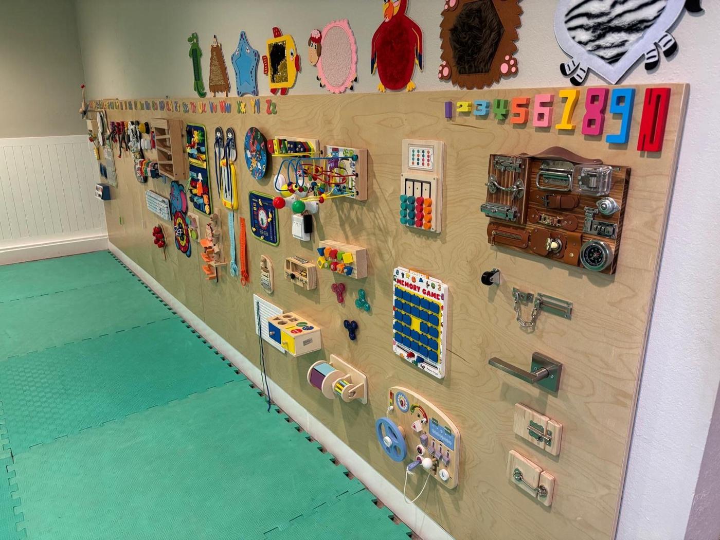 A long wooden wall of hands-on activity panels above green foam floor mats
